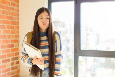 Genç Asyalı bir kadın tatlı, eğlenceli, mutlu, sevimli bir ifadeyle dudaklarını birbirine bastırıyor. Öpücük yolluyor.