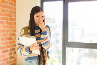 Genç Asyalı kadın iğreniyor, kötü ve nahoş bir koku duymamak için burnunu tutuyor.
