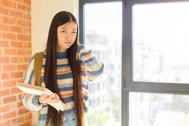 Asyalı genç bir kadın stresli, hayal kırıklığına uğramış ve yorgun hissediyor. Endişeli ve sorunlu bir bakışla boynunu ovalıyor.