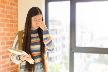 Genç Asyalı kadın stresli, mutsuz ve hayal kırıklığına uğramış, alınına dokunmuş ve şiddetli baş ağrısı çeken.