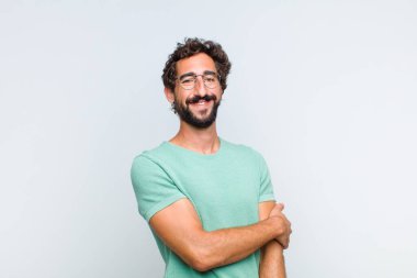 Genç sakallı adam utangaç ve neşeli bir şekilde gülüyor, arkadaş canlısı ve olumlu ama güvensiz bir tavırla.