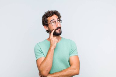 Genç sakallı adam mutlu bir şekilde gülümsüyor ve hayal kuruyor ya da şüphe ediyor.