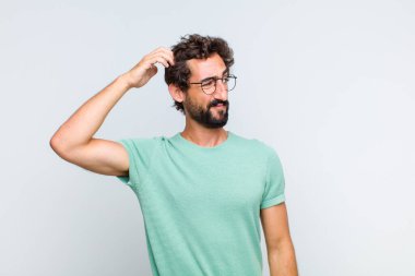 Genç sakallı adam şaşkın ve kafası karışmış hissediyor, başını kaşıyor ve yan tarafa bakıyor.