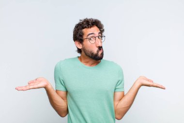 Genç sakallı adam şaşkın ve şaşkın hissediyor, şüpheci, farklı seçenekleri tartıyor veya komik bir ifadeyle seçiyor.