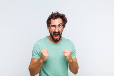 Genç sakallı adam sinirli, sinirli, sinirli bakışlar ve sıkı yumruklar ile agresif bir şekilde bağırıyor.