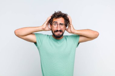 Genç sakallı adam kendini stresli, endişeli ya da korkmuş hissediyor. Elleri başının üstünde, hatayla panikliyor.