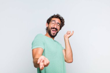 Genç sakallı adam gülümsüyor, tasasız hissediyor, rahat ve mutlu, dans ediyor ve müzik dinliyor, bir partide eğleniyor.