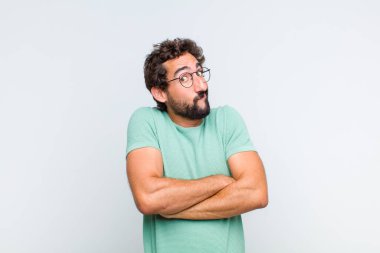 Genç sakallı adam omuz silkiyor, kafası karışık ve emin değil, kolları bağlı ve şaşkın görünüyor.