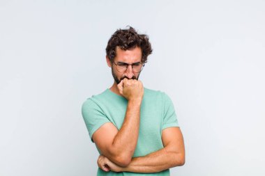 Genç sakallı adam ciddi, düşünceli ve endişeli hissediyor, elleri çenesine bastırılmış, yan bakıyor.