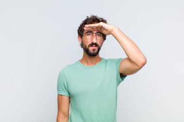 Genç sakallı adam şaşkın ve şaşkın bakıyor, el üstünde uzak bakıyor, izliyor ya da arıyor