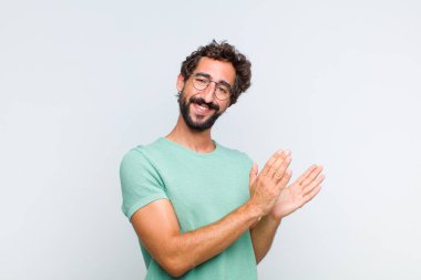 Genç sakallı adam mutlu ve başarılı hissediyor, gülümsüyor ve alkışlıyor, alkışlarla tebrik ediyor.