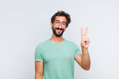 Genç sakallı adam gülümsüyor ve arkadaş canlısı görünüyor. İki ya da iki numarayı gösteriyor. Elleri önde, geriye doğru sayıyor.