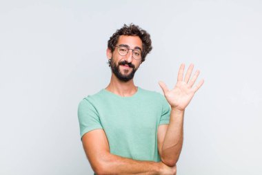 Genç sakallı adam gülümsüyor ve arkadaş canlısı görünüyor. 5 ya da 5 numarayı gösteriyor.