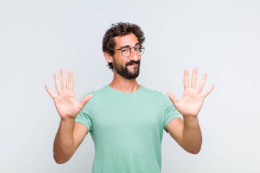 Genç sakallı adam gülümsüyor ve arkadaş canlısı görünüyor, onuncu veya onuncu numarayı gösteriyor, eli önde, geriye doğru sayıyor.