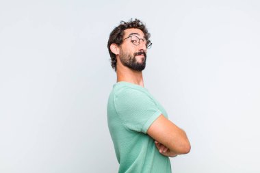 Genç sakallı adam neşeyle gülümsüyor, mutlu, tatmin olmuş ve rahatlamış hissediyor, kollarını kavuşturup yan tarafa bakıyor.