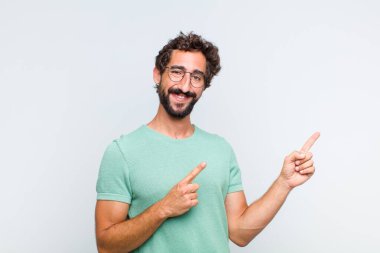 Genç sakallı adam mutlu bir şekilde gülümsüyor ve her iki elinde fotokopi alanında nesne gösteriyor.