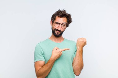 Genç sakallı adam sabırsız ve kızgın görünüyor, saati gösteriyor, dakiklik istiyor, zamanında gelmek istiyor.