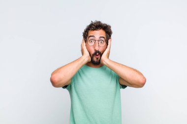Genç sakallı adam heyecanlı ve şaşırmış görünüyor, ağzı açık, iki eli de başında, kendini şanslı bir kazanan gibi hissediyor.