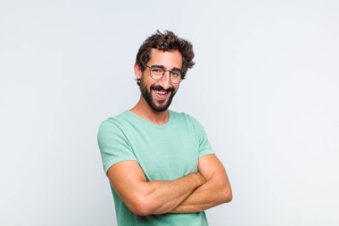 Genç sakallı adam mutlu, gururlu ve tatmin olmuş görünüyor. Kollarını kavuşturup gülümsüyor.