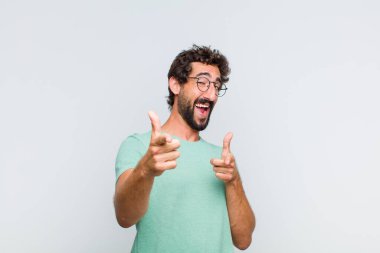 Olumlu, başarılı, mutlu bir tavırla gülümseyen genç sakallı adam kamerayı işaret ederek, elleriyle silah işareti yapıyor.
