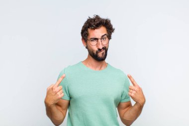 Kötü tavırlı genç sakallı adam gururlu ve agresif görünüyor, yukarıyı işaret ediyor ya da elleriyle alay işareti yapıyor.