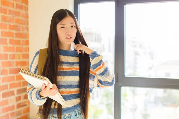 Asyalı genç bir kadın stresli, endişeli, yorgun ve hayal kırıklığına uğramış, gömleğini çekmiş, sorunlu görünüyor.