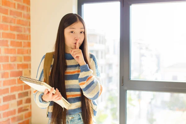 Genç Asyalı kadın sessizlik ve sessizlik istiyor, parmaklarıyla ağzının önünde işaret ediyor, 