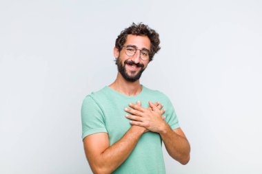 Genç sakallı adam romantik, mutlu ve aşık, neşeyle gülümsüyor ve kalbe yakın el ele tutuşuyor.