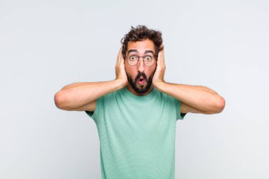 Genç sakallı adam hoş olmayan bir şekilde şok olmuş, korkmuş ya da endişeli görünüyor ağzı sonuna kadar açık ve iki kulağını da elleriyle kapatıyor.