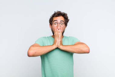 Genç sakallı adam endişeli, üzgün ve korkmuş hissediyor, elleriyle ağzını kapatıyor, endişeli ve berbat görünüyor.