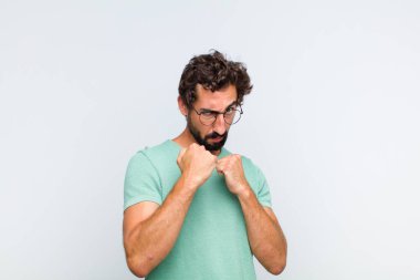 Genç sakallı adam kendinden emin, sinirli, güçlü ve agresif görünüyor. Yumrukları boks pozisyonunda dövüşmeye hazır.