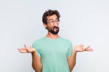 young bearded man shrugging with a dumb, crazy, confused, puzzled expression, feeling annoyed and clueless