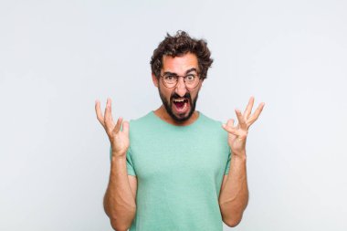 Genç sakallı adam elleri havada bağırıyor. Öfkeli, sinirli, stresli ve üzgün.