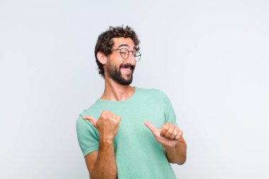 Genç sakallı adam neşeyle gülümsüyor ve yan taraftaki fotokopi alanını gösteriyor, mutlu ve tatmin olmuş hissediyor.