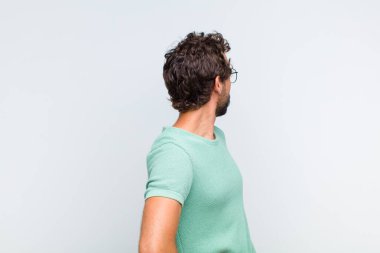 Genç sakallı adam kafası karışık ya da dolgun hissediyor ya da şüphe ve sorular, merak ediyor, elleri kalçasında, dikiz aynasından.