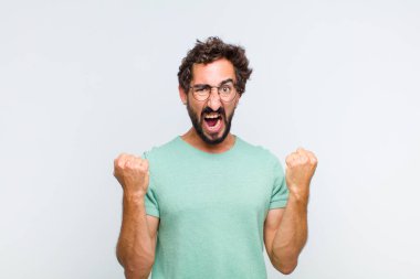 Genç sakallı adam sinirli bir ifadeyle ya da yumruklarıyla başarıyı kutlarken agresif bir şekilde bağırıyor.