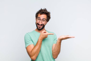 Genç sakallı adam neşeyle gülümsüyor ve yan taraftaki fotokopi alanını işaret ediyor, bir nesneyi gösteriyor ya da reklamını yapıyor.