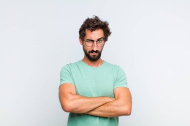 Genç sakallı adam hayal kırıklığına uğramış ve hayal kırıklığına uğramış hissediyor. Ciddi görünüyor, kızgın ve kollarını kavuşturmuş.