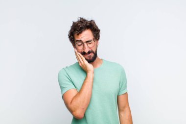 Genç sakallı adam yanağını tutuyor ve acı veren diş ağrısı çekiyor, hasta, sefil ve mutsuz hissediyor, dişçi arıyor