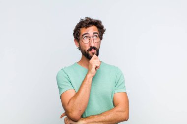 Genç sakallı adam düşünceli, meraklı ya da hayal kuruyor, hayal kuruyor ve mekanı kopyalamak için yukarı bakıyor.