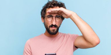 Genç sakallı adam şaşkın ve şaşkın bakıyor, el üstünde uzak bakıyor, izliyor ya da arıyor