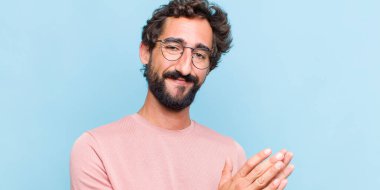 Genç sakallı adam mutlu ve başarılı hissediyor, gülümsüyor ve alkışlıyor, alkışlarla tebrik ediyor.