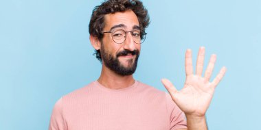 Genç sakallı adam gülümsüyor ve arkadaş canlısı görünüyor. 5 ya da 5 numarayı gösteriyor.