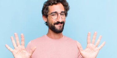 Genç sakallı adam gülümsüyor ve arkadaş canlısı görünüyor, onuncu veya onuncu numarayı gösteriyor, eli önde, geriye doğru sayıyor.