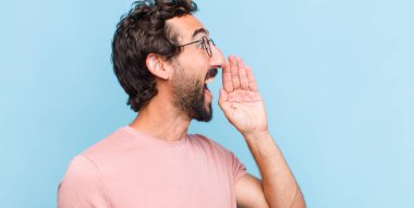 Genç sakallı adam profili, mutlu ve heyecanlı görünüyor, bağırıyor ve kenardaki boşluğu kopyalamak için arıyor.