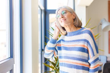 Orta yaşlı bir kadın ciddi ve meraklı görünüyor, dinliyor, gizli bir konuşma veya dedikodu duymaya çalışıyor, kulak misafiri oluyor.