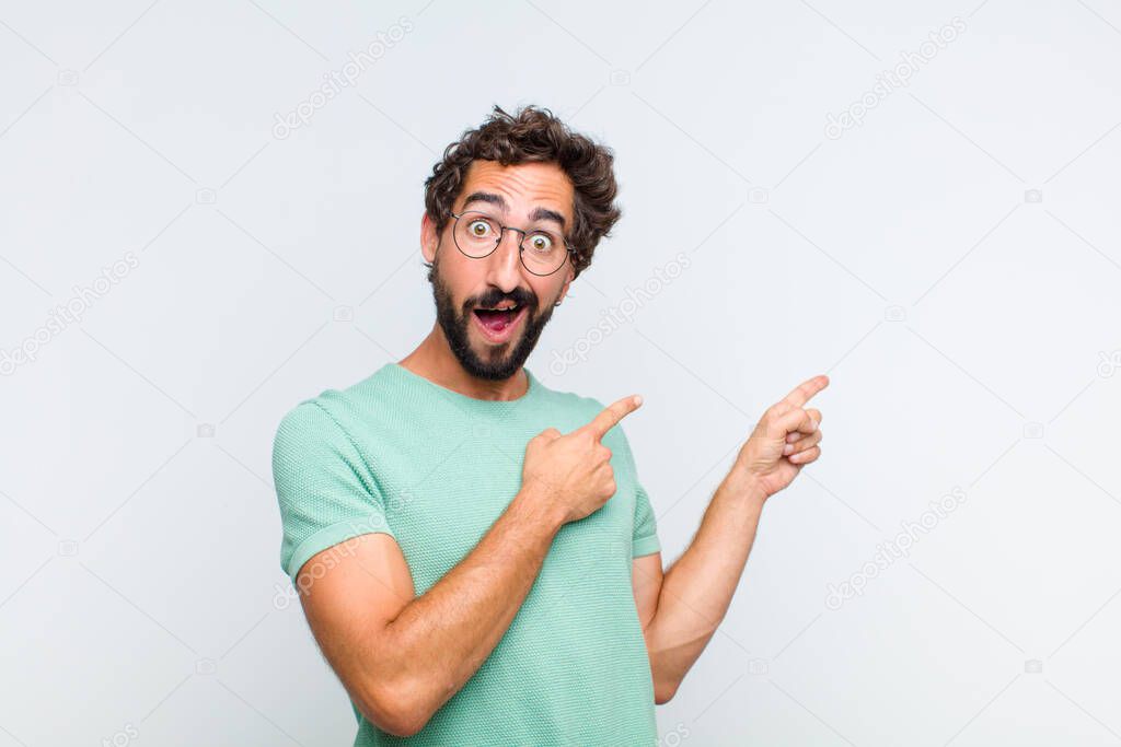 young bearded man feeling joyful and surprised, smiling with a shocked expression and pointing to the side