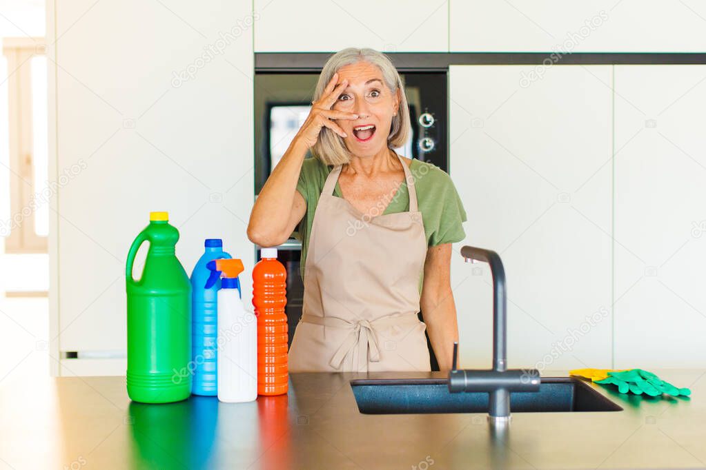 middle age woman looking shocked, scared or terrified, covering face with hand and peeking between fingers