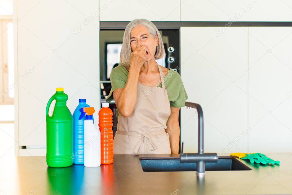 middle age woman feeling disgusted, holding nose to avoid smelling a foul and unpleasant stench