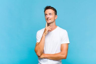 Genç yakışıklı adam mutlu bir şekilde gülümsüyor ve hayal kuruyor ya da şüphe ediyor.